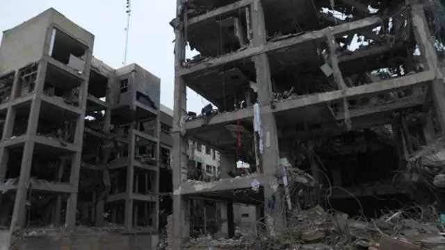 يظهر مبنيان مدمران، يتألف كل منهما من أربعة إلى خمسة طوابق، وقد تناثرت نوافذهما وتهدّمت جدرانهما. ولا تزال بعض الأعمدة الخرسانية وأجزاء من الطوابق قائمة. وتتدلى قطع من الأقمشة من الهيكل، فيما تنتشر قطع من المعدن الملتوي على الأرض.
